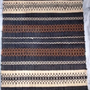 May include: A black, brown, and cream striped woven rug with fringe on the ends. The rug has a geometric pattern.