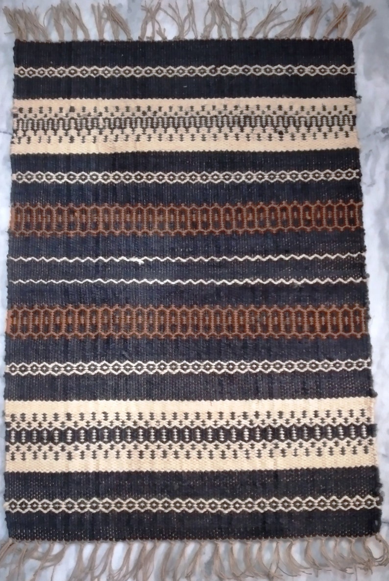 May include: A black, brown, and cream striped woven rug with fringe on the ends. The rug has a geometric pattern.
