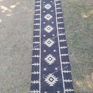 May include: Black and white geometric patterned rug with fringe. The rug is made of jute and has a distressed look. The rug is approximately 2.5 feet wide and 8 feet long.