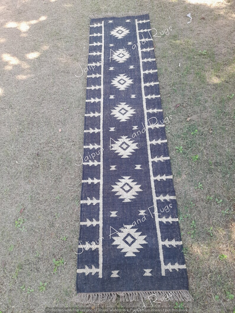 May include: Black and white geometric patterned rug with fringe. The rug is made of jute and has a distressed look. The rug is approximately 2.5 feet wide and 8 feet long.