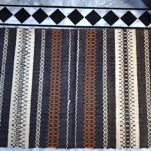 May include: A woven rug with a striped pattern in shades of brown, black, and white. The rug has a fringe on both ends.