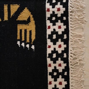 Puede incluir: Alfombra negra y blanca con un patr&oacute;n geom&eacute;trico y acentos rojos. La alfombra tiene un borde de flecos.