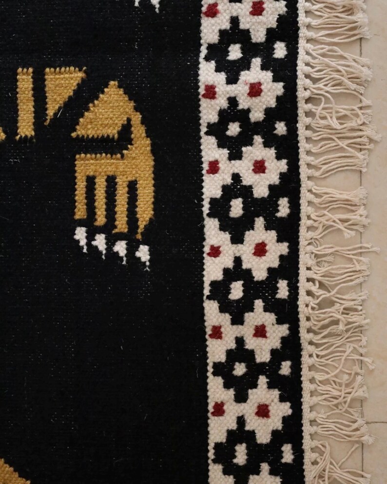 Puede incluir: Alfombra negra y blanca con un patr&oacute;n geom&eacute;trico y acentos rojos. La alfombra tiene un borde de flecos.