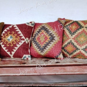 May include: Four decorative throw pillows with a geometric pattern in shades of red, brown, beige, and green. The pillows are arranged on a wooden bench.