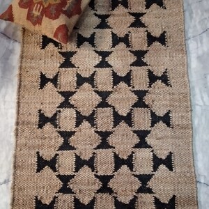 May include: A rectangular jute rug with a geometric pattern of black diamonds and stars. The rug has a natural, earthy tone.