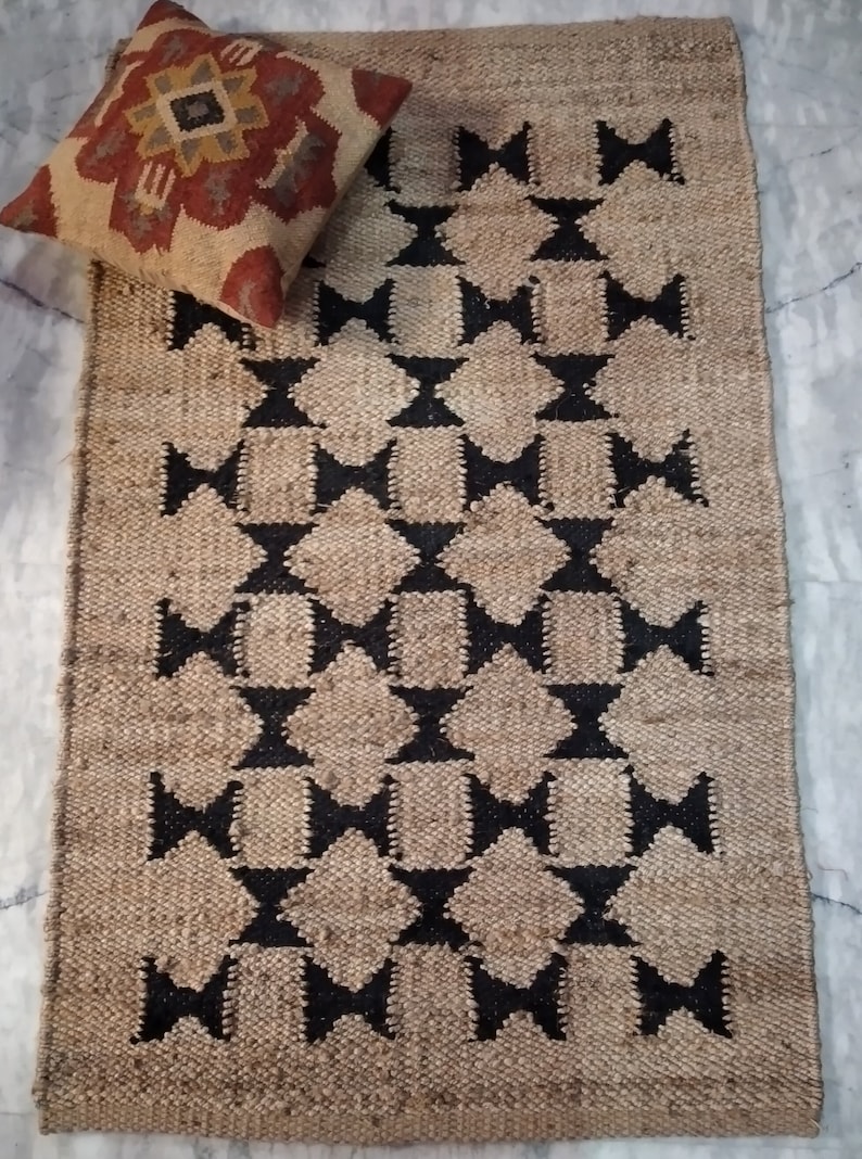 May include: A rectangular jute rug with a geometric pattern of black diamonds and stars. The rug has a natural, earthy tone.