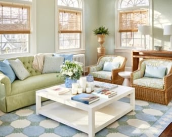 May include: A light green sofa with pillows and a white coffee table in a living room with two wicker chairs, a rug, and large windows with blinds.