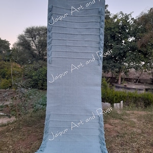 May include: A light blue handwoven rug with fringe on both ends. The rug is held up by a person, and the text "Jaipur Art and Rugs" is visible on the rug.