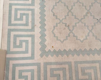 May include: A rectangular area rug featuring a light blue Greek key border pattern on a cream background. The central section displays a repeating geometric lattice design outlined in light blue, separated from the border by a zigzag line.