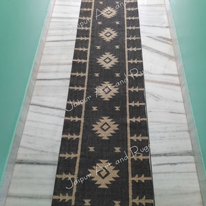 May include: Black and white geometric patterned rug with fringe on the ends. The rug has a tribal design with a black background and white geometric shapes.