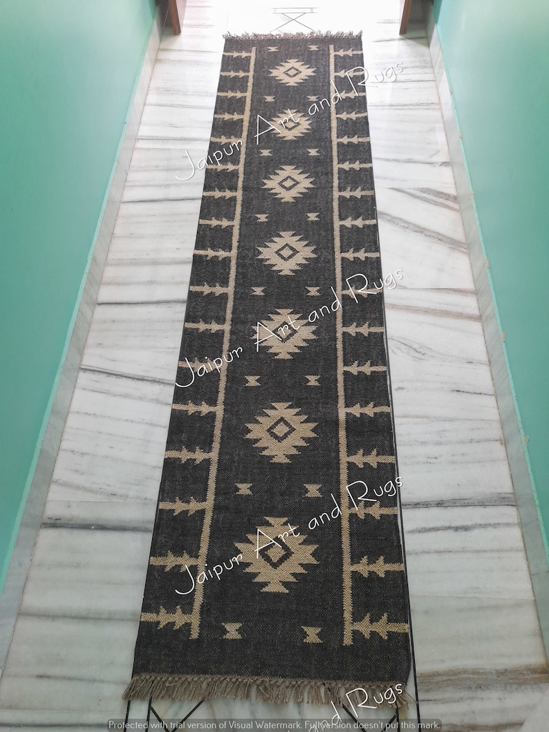 May include: Black and white geometric patterned rug with fringe on the ends. The rug has a tribal design with a black background and white geometric shapes.