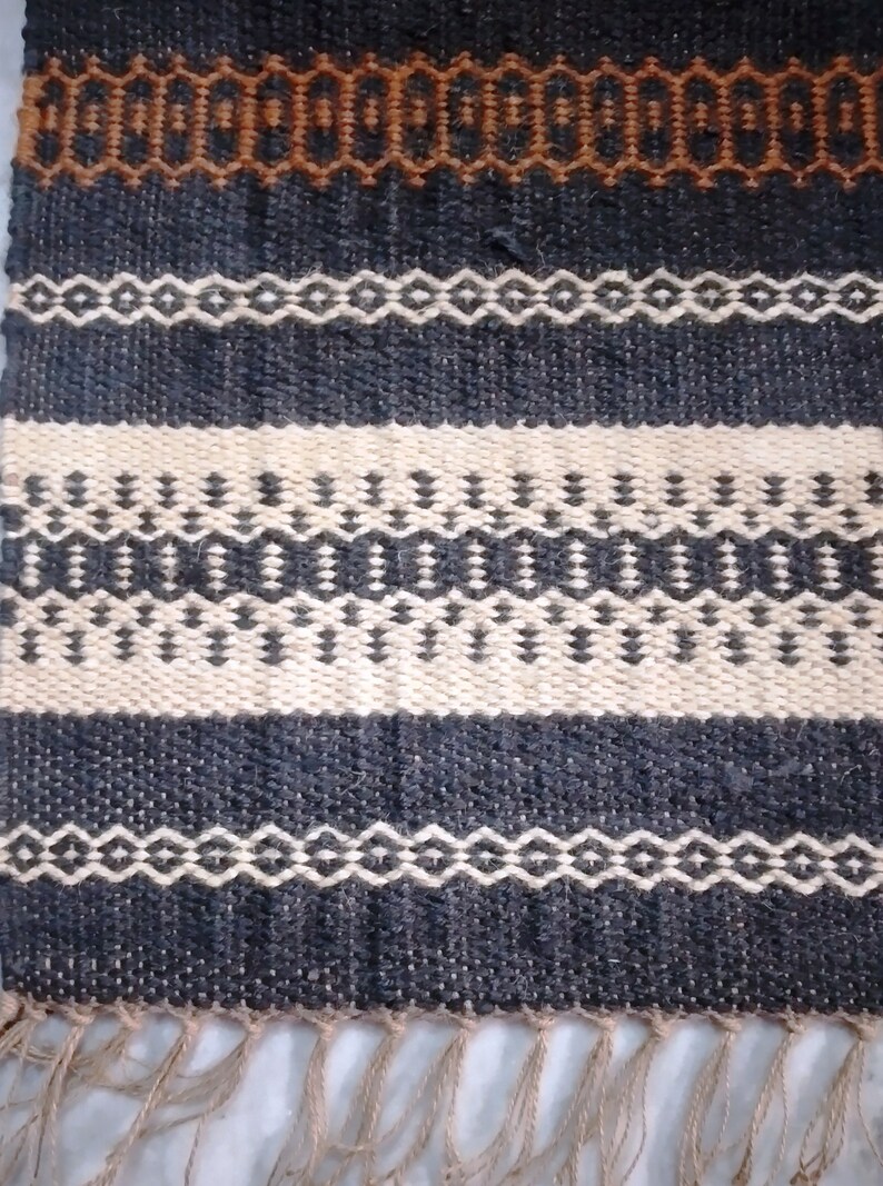 May include: A woven rug with a geometric pattern in shades of brown, black, and white. The rug has a fringe on the bottom edge.