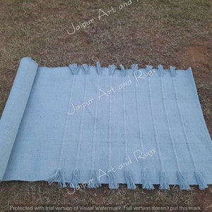 May include: A light blue woven rug with fringe on the ends. The rug is rolled up on the left side of the image.
