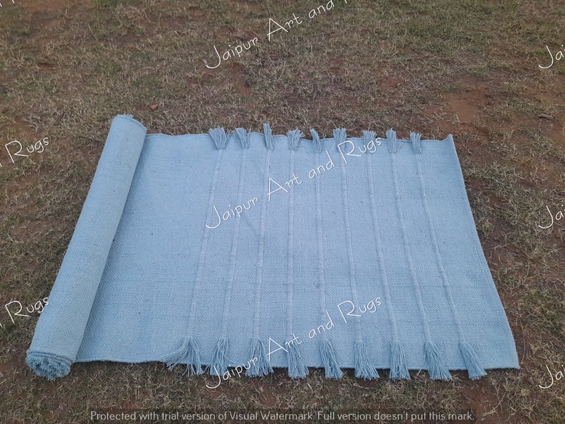 May include: A light blue woven rug with fringe on the ends. The rug is rolled up on the left side of the image.