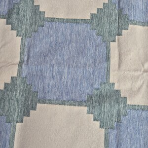 May include: A textile fabric featuring a repeating geometric pattern of large squares in light beige and medium blue. The squares are separated by dark teal cross-shaped accents with a stepped, pixelated edge design throughout the material.