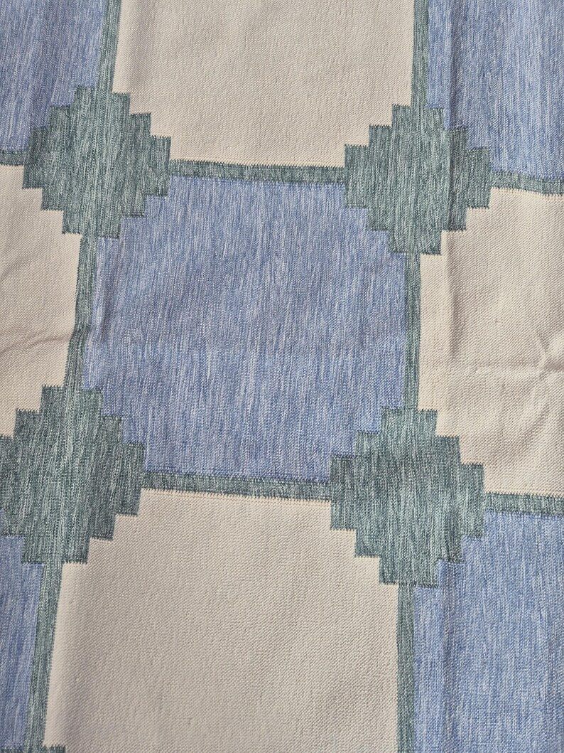 May include: A textile fabric featuring a repeating geometric pattern of large squares in light beige and medium blue. The squares are separated by dark teal cross-shaped accents with a stepped, pixelated edge design throughout the material.