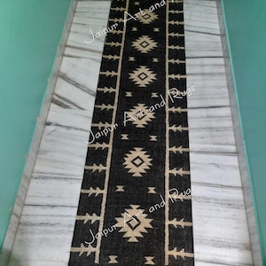 May include: Black and cream geometric patterned rug with fringe on the ends. The rug is laid out on a white marble floor.