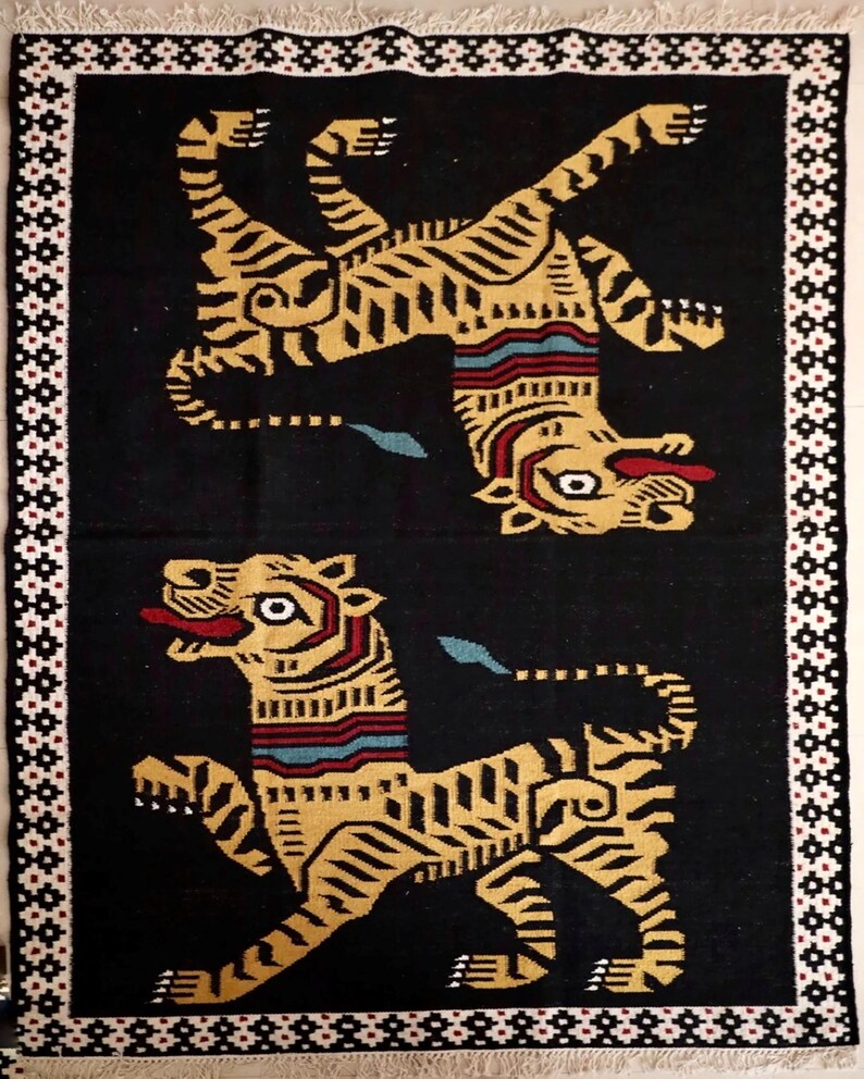 Puede incluir: Una alfombra negra con un borde blanco presenta dos tigres amarillos estilizados con rayas negras. Los tigres est&aacute;n mirando en direcciones opuestas y tienen un dise&ntilde;o geom&eacute;trico.