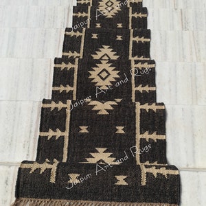 May include: A set of five black and beige patterned jute rugs with fringe. The rugs are arranged in a staircase pattern. The text "Jaipur Art and Rugs" is printed on the rugs.