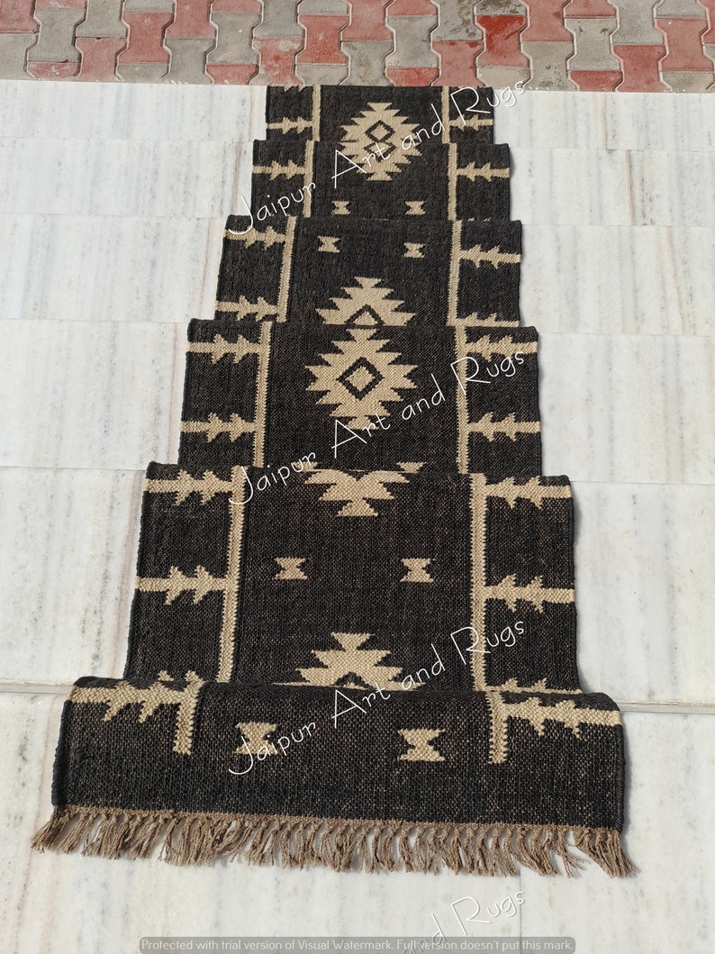 May include: A set of five black and beige patterned jute rugs with fringe. The rugs are arranged in a staircase pattern. The text "Jaipur Art and Rugs" is printed on the rugs.