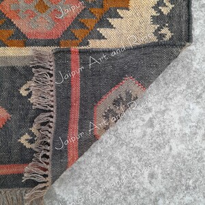 May include: Close-up of the corner of a black, brown, and cream handwoven rug with fringe. The rug has a geometric pattern and the text "Jaipur Art and Rugs" is visible in the image.