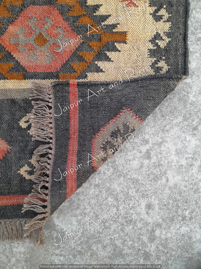May include: Close-up of the corner of a black, brown, and cream handwoven rug with fringe. The rug has a geometric pattern and the text "Jaipur Art and Rugs" is visible in the image.