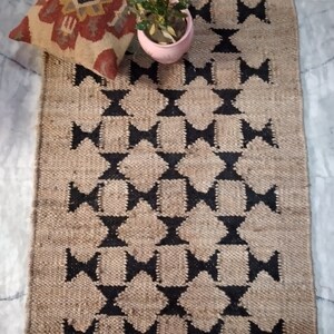 May include: A brown and black jute rug with a geometric pattern. The rug has a diamond shape with a black outline and a brown center. The rug is made of natural fibers and has a rustic look.