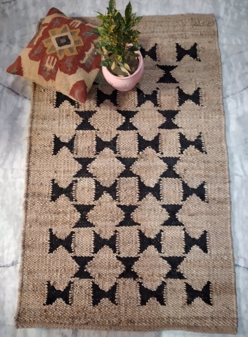 May include: A brown and black jute rug with a geometric pattern. The rug has a diamond shape with a black outline and a brown center. The rug is made of natural fibers and has a rustic look.