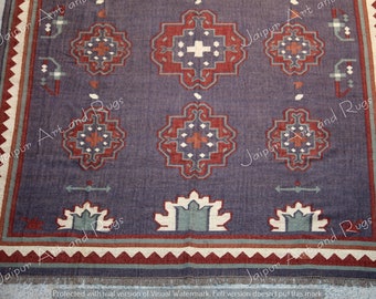 May include: A rectangular area rug featuring a dark purple base with a repeating geometric pattern of red and cream-colored cross-shaped motifs. The border displays a zigzag pattern in red and cream, with additional green and cream floral-like shapes.