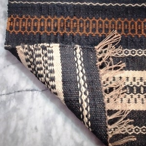 May include: A black and white striped rug with brown accents. The rug has a fringe on the bottom edge and is folded over on itself.