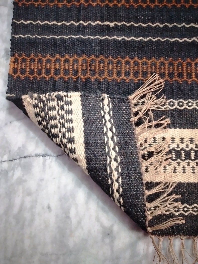 May include: A black and white striped rug with brown accents. The rug has a fringe on the bottom edge and is folded over on itself.