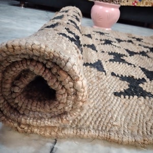 May include: A rolled-up jute rug with a black and white geometric pattern. The rug is made of natural fibers and has a rustic look.