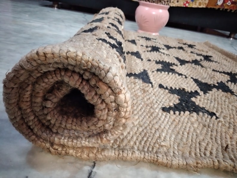 May include: A rolled-up jute rug with a black and white geometric pattern. The rug is made of natural fibers and has a rustic look.