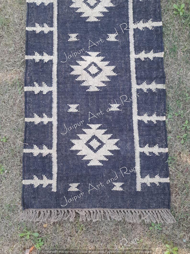 May include: A black and white geometric patterned rug with fringe. The rug has a dark blue background with a white geometric pattern. The rug is made of cotton and is perfect for adding a touch of style to any room.
