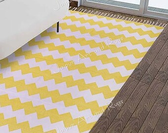 May include: A yellow and white chevron patterned rug with fringe on the edges. The rug is on a wooden floor.