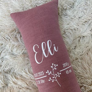 May include: A dusty rose rectangular pillow with the name "Elli" in white script. The pillow also features the birth date, time, weight (2810 g), and length (49 cm) in white text, along with a floral design.