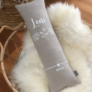 May include: A grey rectangular pillow with white text and a floral design. The text includes the name "Leni", date, time, and measurements. The pillow is resting on a white fluffy surface.