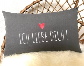 Könnte beinhalten: Ein graues rechteckiges Kissen mit weißem Text, der "ICH LIEBE DICH!" lautet, und einem roten Herzen.