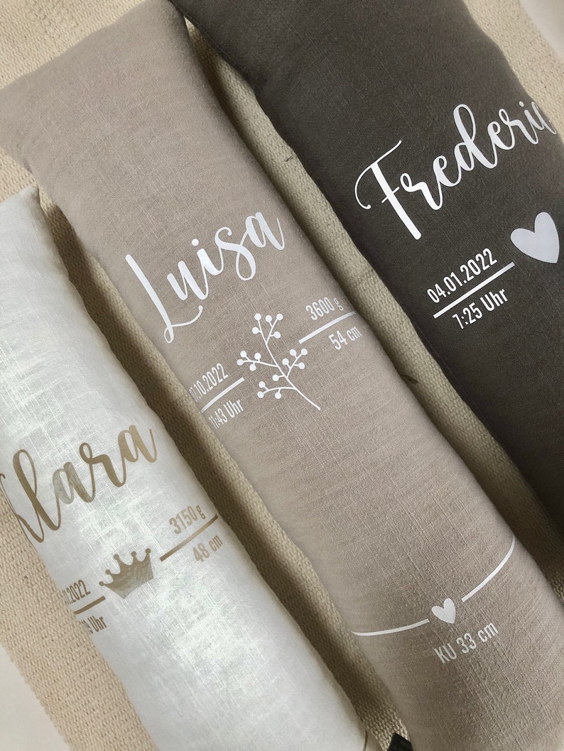 May include: Three long, rectangular pillows in white, beige, and dark grey. Each pillow features a name in a script font, alongside birth details including weight in grams, length in centimetres, and the time and date of birth.