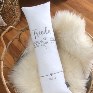 May include: A white rectangular pillow with the name "Frieda" printed in silver script, along with birth details. The pillow is 50 cm long and weighs 3070 grams. It rests on a fluffy white sheepskin rug.