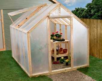 May include: A wooden framed greenhouse with a clear plastic covering. The greenhouse has a hinged door and a small window that can be opened for ventilation. There is a wooden shelf inside the greenhouse with potted plants.