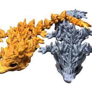 May include: Two 3D printed lizard figurines, one gold and one silver, with spiky, detailed scales and a textured finish.