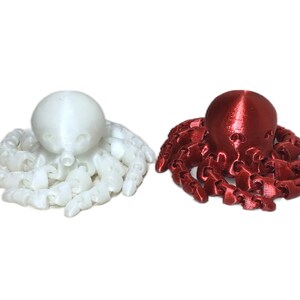 Puede incluir: Dos figuritas de pulpo impresas en 3D, una blanca y otra roja.