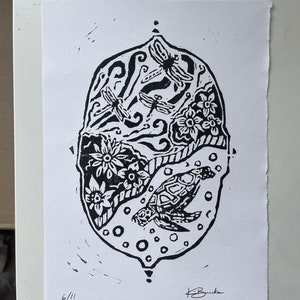 May include: Black and white linocut print of a turtle and dragonflies in a circle with a floral design. The print is numbered 6/11 and signed "H. Burke".