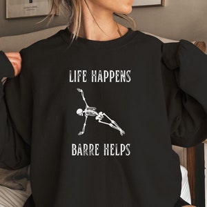 May include: Black sweatshirt with a white skeleton doing a barre pose and the text "Life Happens Barre Helps".