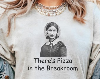May include: A light gray t-shirt with a black and white image of a woman wearing a nurse's uniform. The text "There's Pizza in the Breakroom" is printed below the image.