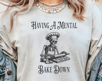 May include: A gray sweatshirt with the text "Having a mental bake down" and a black and white illustration of a skeleton wearing a chef's hat and apron, rolling out dough.