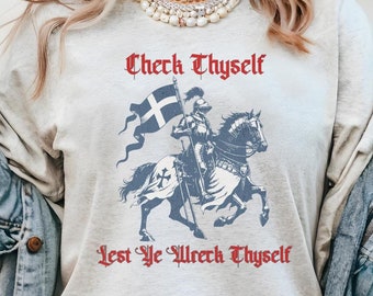 Può includere: Una maglietta grigia a maniche lunghe con un'illustrazione vintage di un cavaliere a cavallo che tiene una bandiera. Il testo "Check Thyself Lest Ye Wreck Thyself" è stampato in rosso sulla maglietta.