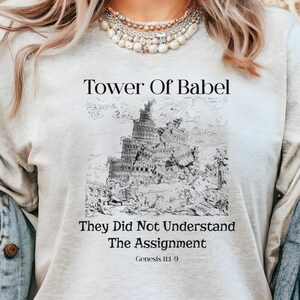 Könnte beinhalten: Hellgraues T-Shirt mit einer Schwarz-Weiß-Illustration des Turms zu Babel. Der Text "Tower Of Babel" steht über dem Bild, mit "They Did Not Understand The Assignment" und "Genesis 11:9" darunter.