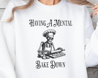 May include: White sweatshirt with a black and white illustration of a skeleton wearing a chef's hat and apron, rolling out dough. The text "HAVING A MENTAL BAKE DOWN" is printed on the sweatshirt.